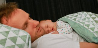 Een vader met zijn baby die op hem slaapt